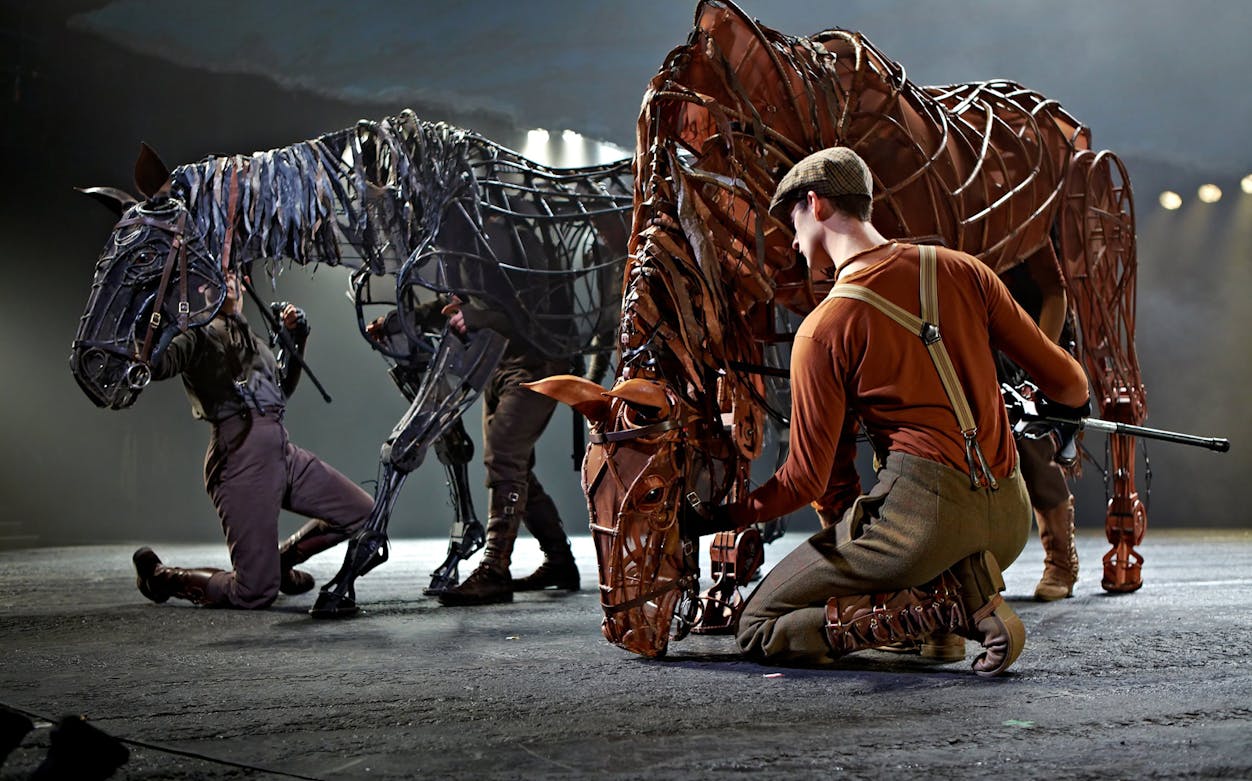 Puppeteers operating life-sized horse puppets in a War Horse stage performance.