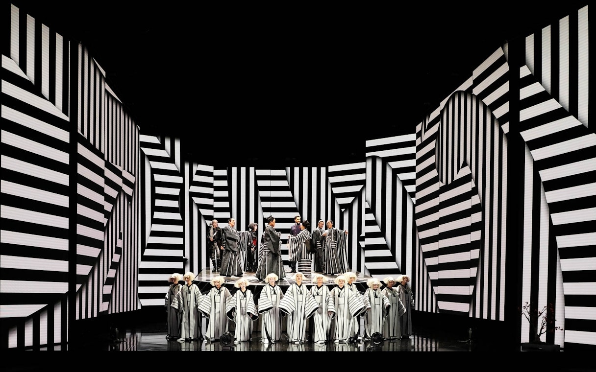 Opera performers on stage with black and white striped set design during Madama Butterfly.