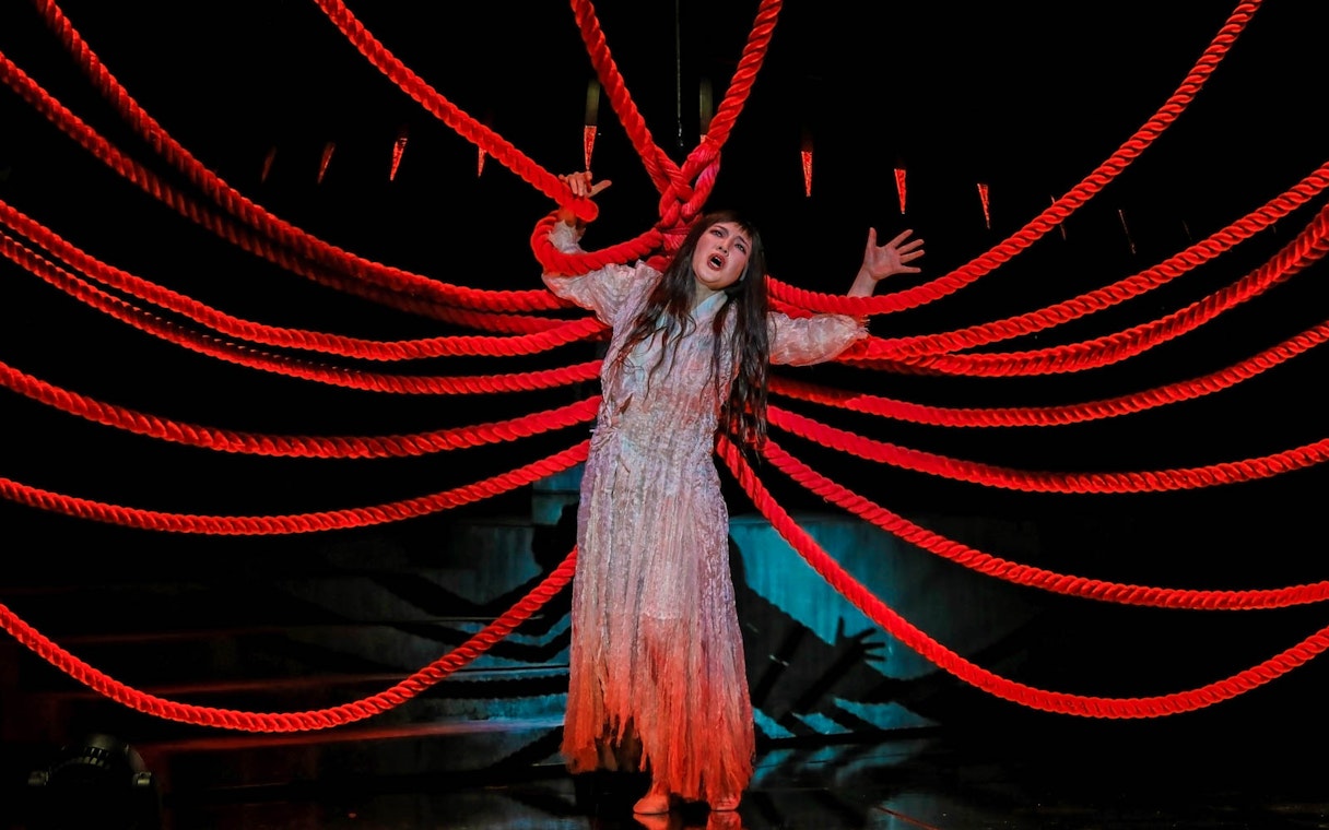 Performer in Madama Butterfly opera with red ropes on stage.
