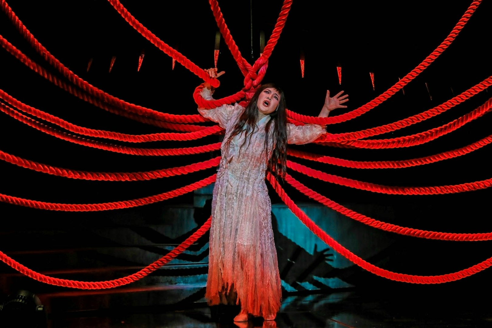 Performer in Madama Butterfly opera with red ropes on stage.