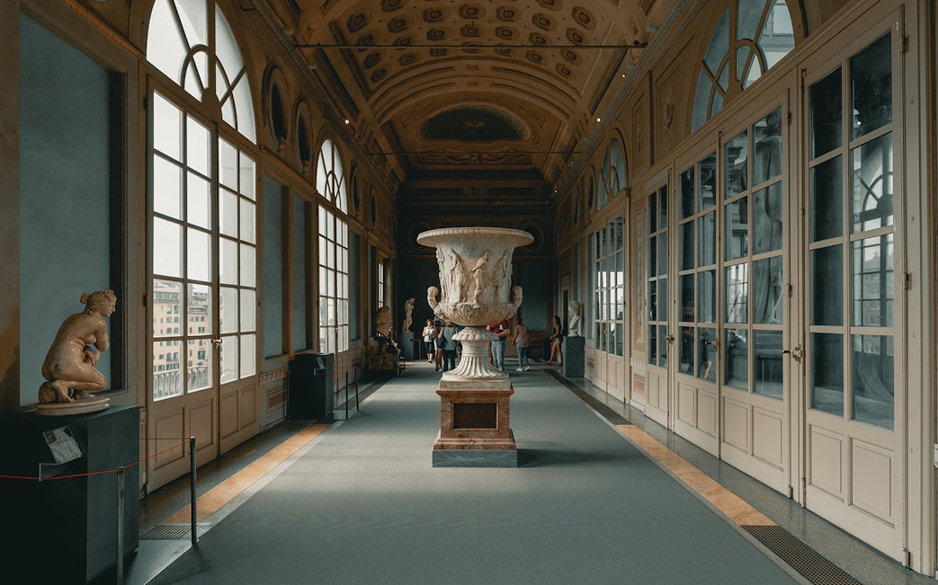 Uffizi Gallery corridor with sculptures and visitors, Florence, Italy.