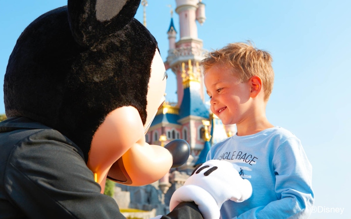 Child meeting character at Disneyland Paris with Sleeping Beauty Castle in background.