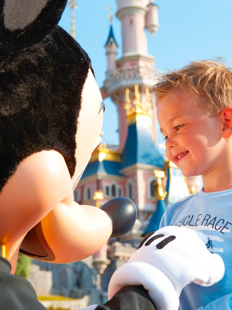 Child meeting character at Disneyland Paris with Sleeping Beauty Castle in background.