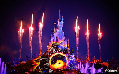Fireworks over illuminated Disney castle at night, featuring Lion King projection.
