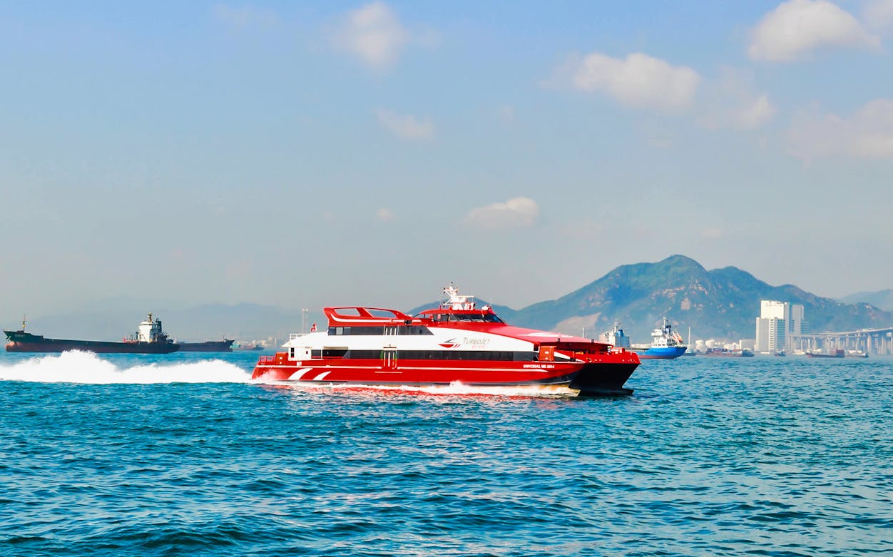 Turbojet ferry on water between Hong Kong Airport and Macau Outer Harbour with mountains in background.