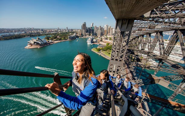 Climbers ascending Sydney Harbour Bridge with Opera House and city skyline in view.