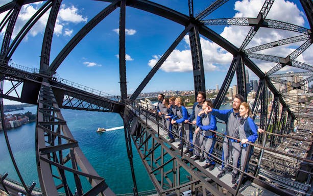 Climbers on Sydney Harbour Bridge with city and water views.