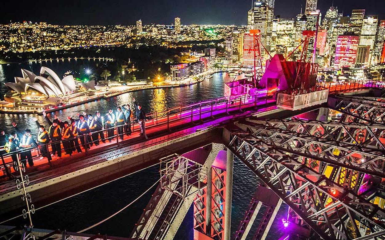 Climbers on Sydney Harbour Bridge at night with city skyline and Opera House.