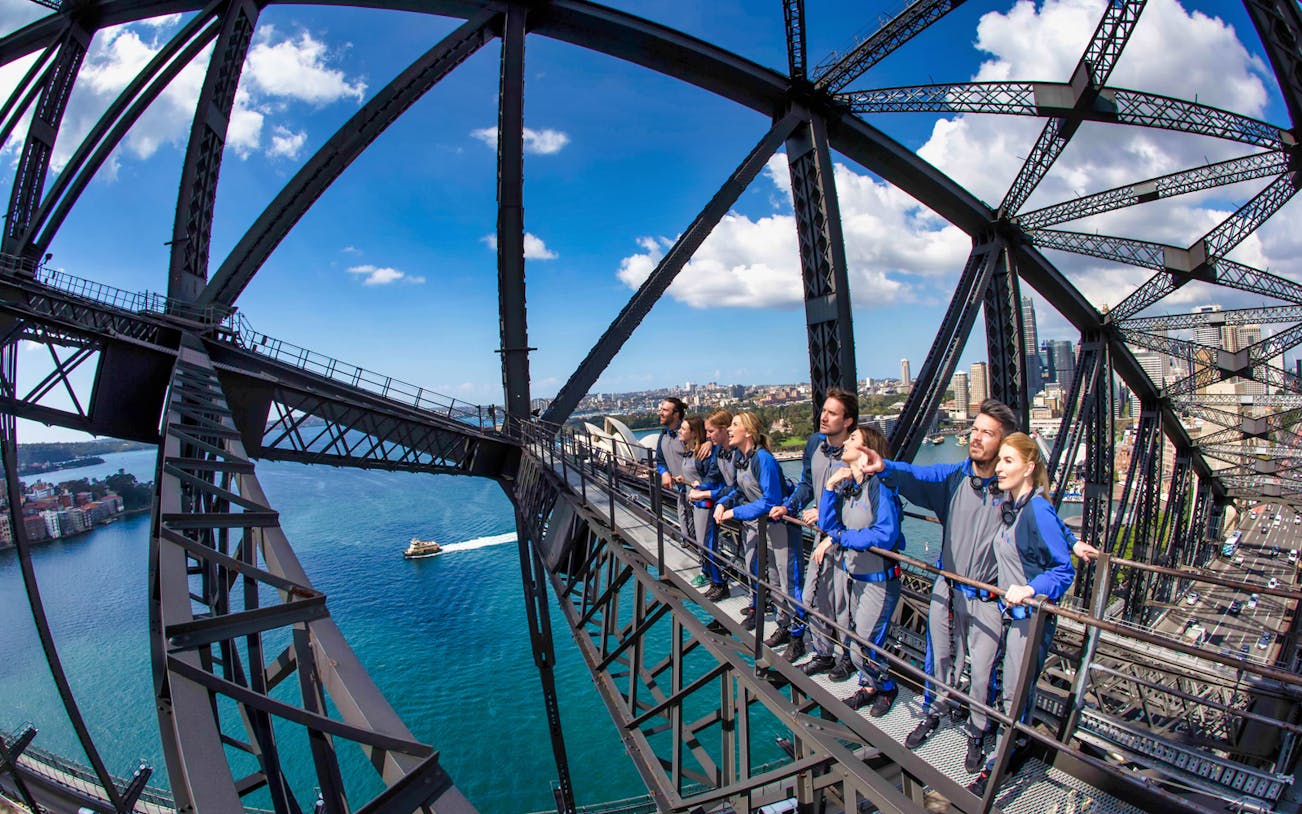 Group climbing Sydney Harbour Bridge with city and water views.