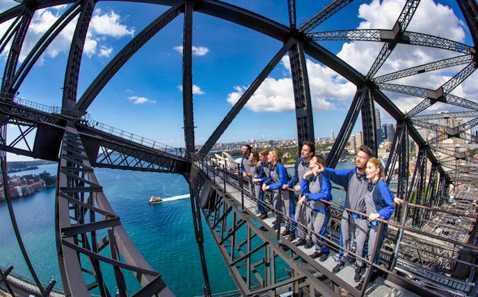 Group climbing Sydney Harbour Bridge with city and water views.