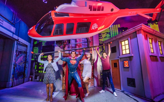 Visitors posing with Superman figure at Madame Tussauds Sydney, holding a helicopter display.