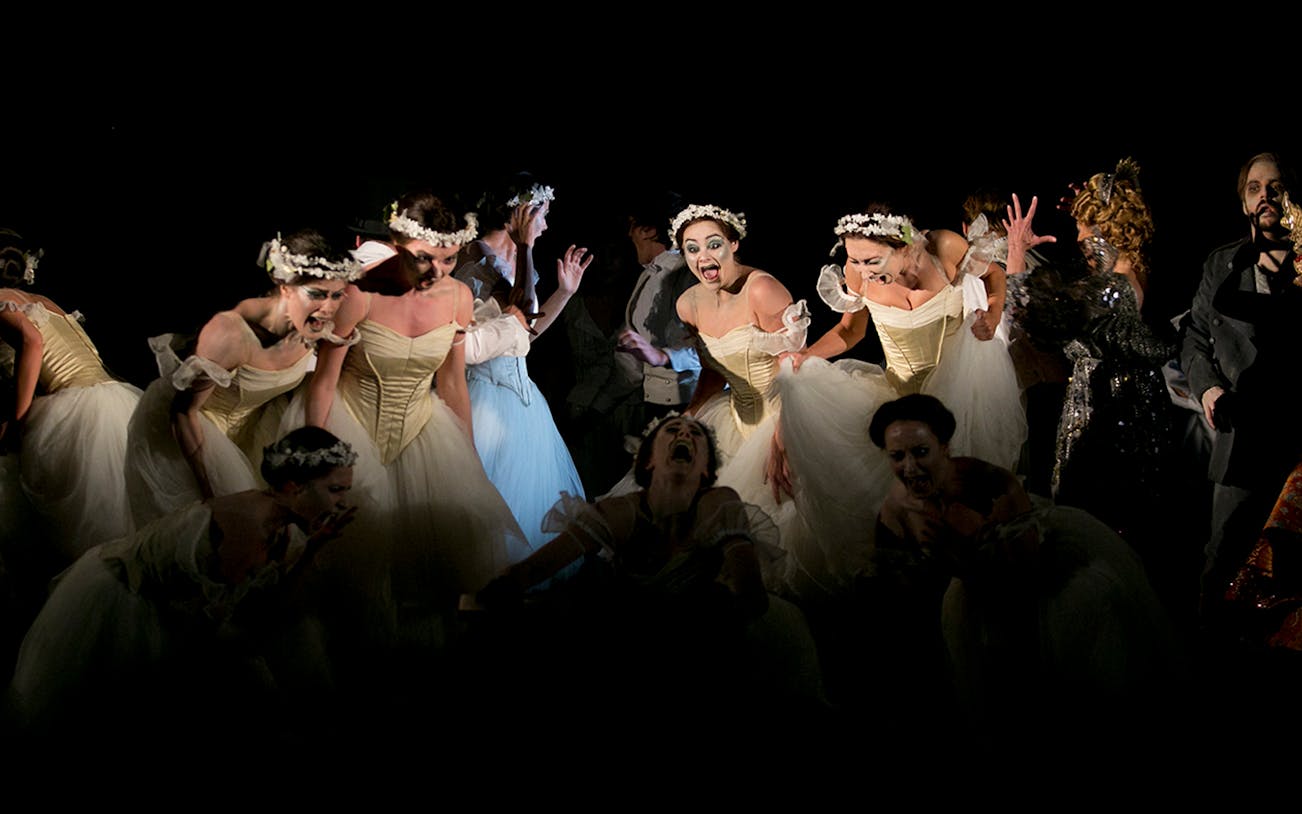 Performers in a dramatic scene from the opera Faust, featuring dancers in white dresses.