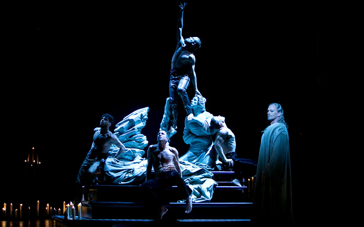 Performers in a dramatic scene from Faust with candles and statues on stage.