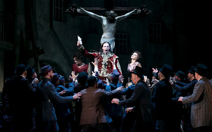 Opera scene from Faust with performers in period costumes, central figure gesturing dramatically.