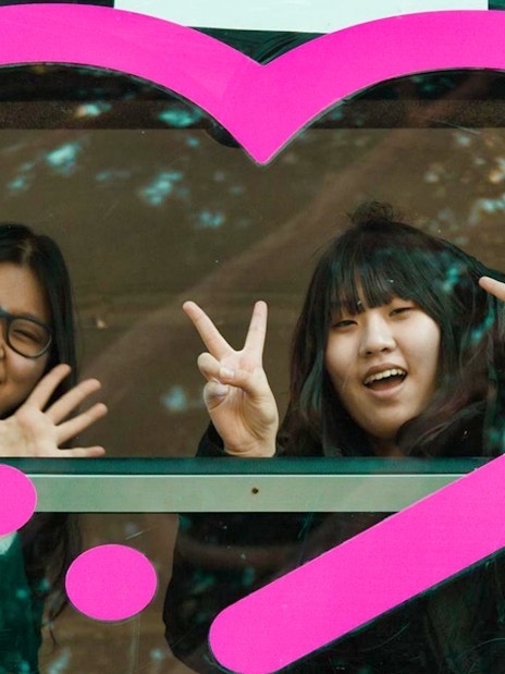 Two people smiling and making peace signs through a bus window with a pink heart design, Rome tour.