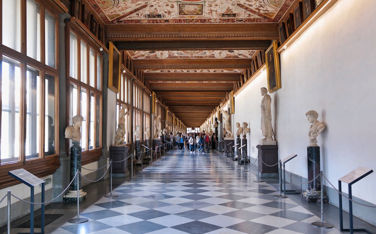 Uffizi Gallery corridor with statues and visitors, Florence, Italy.