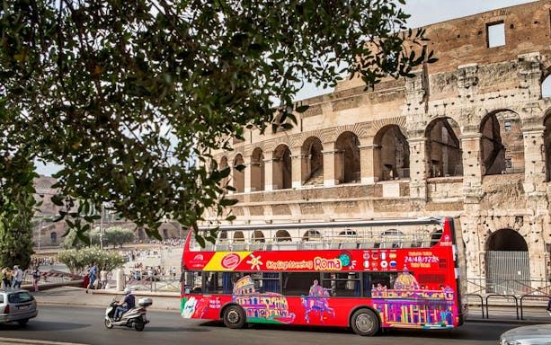 Red hop-on hop-off tour bus in front of the Colosseum in Rome.