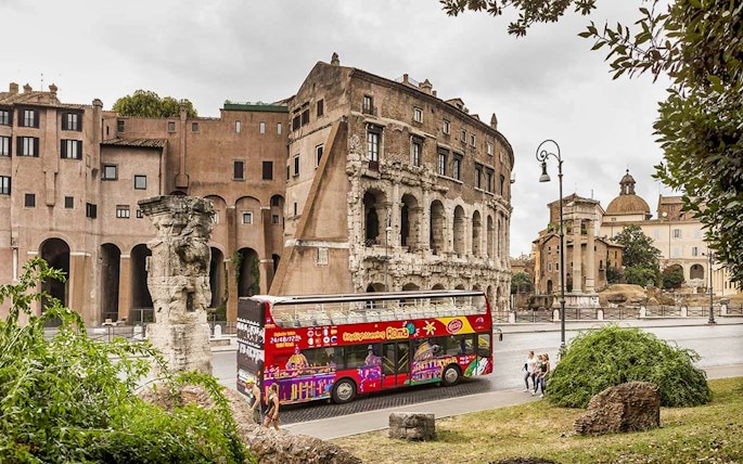 Open-top tour bus near ancient Roman ruins in Rome.