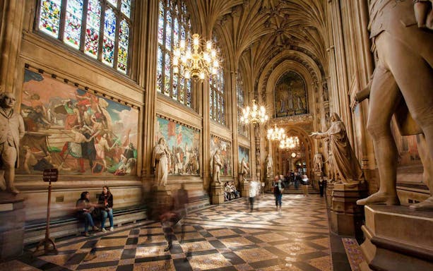 Guided tour inside the ornate halls of Parliament with statues and stained glass windows.