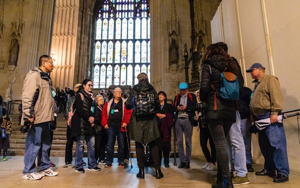 Group of tourists on a guided tour inside a historic parliament building with stained glass windows.