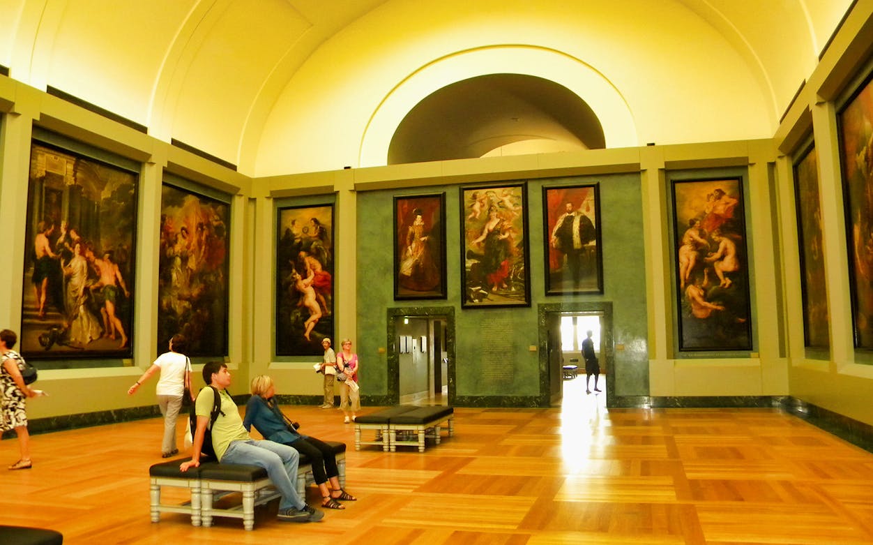 Louvre Museum gallery with visitors viewing large classical paintings.