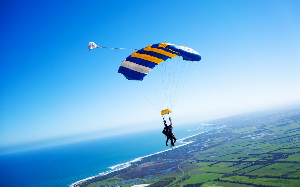 Skydivers tandem freefall over Great Ocean Road coastline.