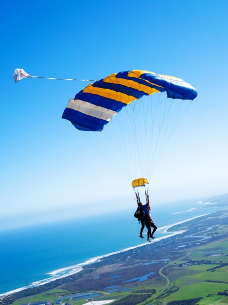 Skydivers tandem freefall over Great Ocean Road coastline.
