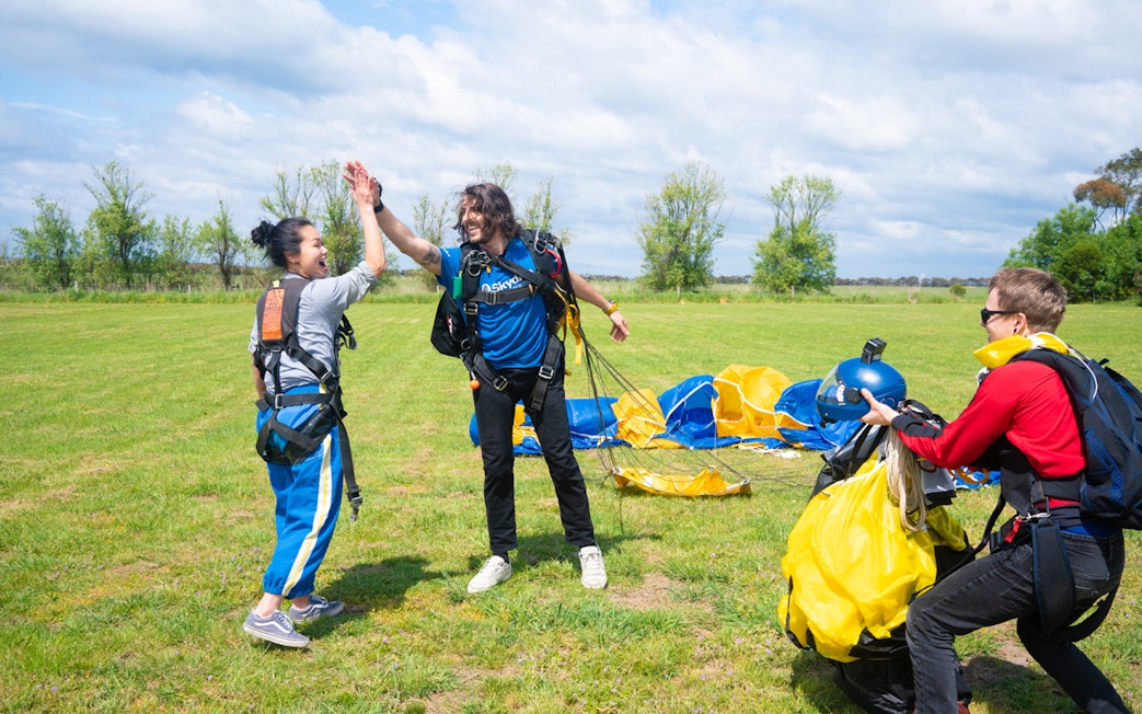 Skydivers celebrate landing on Great Ocean Road with parachutes in the background.