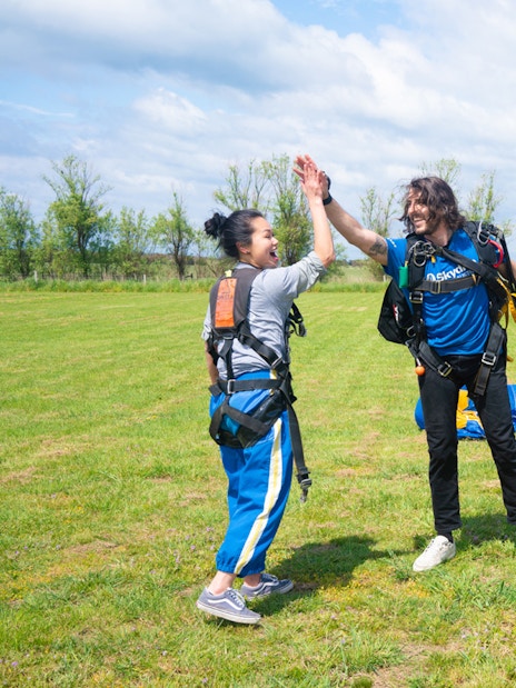 Skydivers celebrate landing on Great Ocean Road with parachutes in the background.