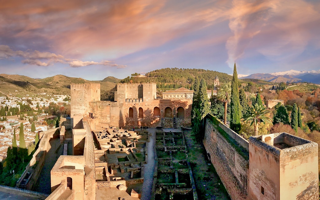 Alhambra fortress with scenic view of Granada, Spain, surrounded by hills and trees.