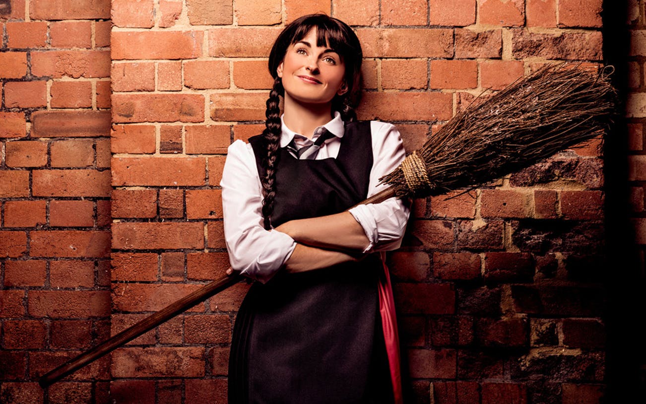 Person in witch costume with broom against brick wall, related to "The Worst Witch.