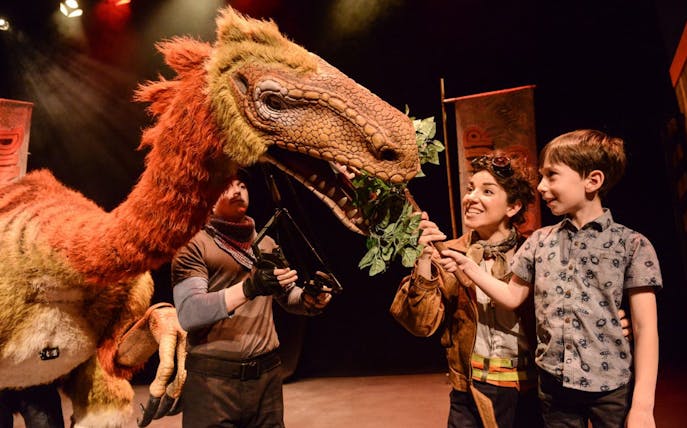 Child interacting with a dinosaur puppet at Dinosaur World Live show.
