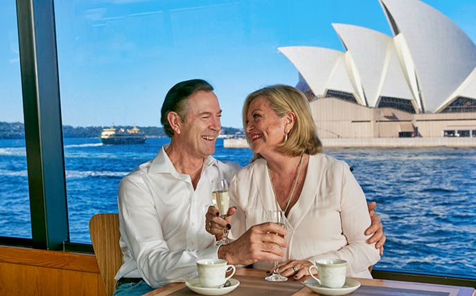 Couple enjoying drinks on Sydney Harbour cruise with Opera House view.
