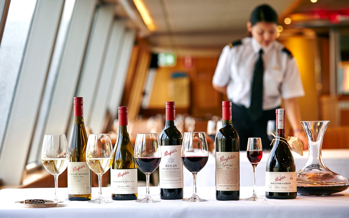 Penfolds wine bottles and glasses on a cruise dining table with a server in the background.