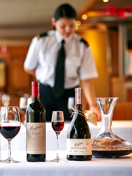 Penfolds wine bottles and glasses on a cruise dining table with a server in the background.