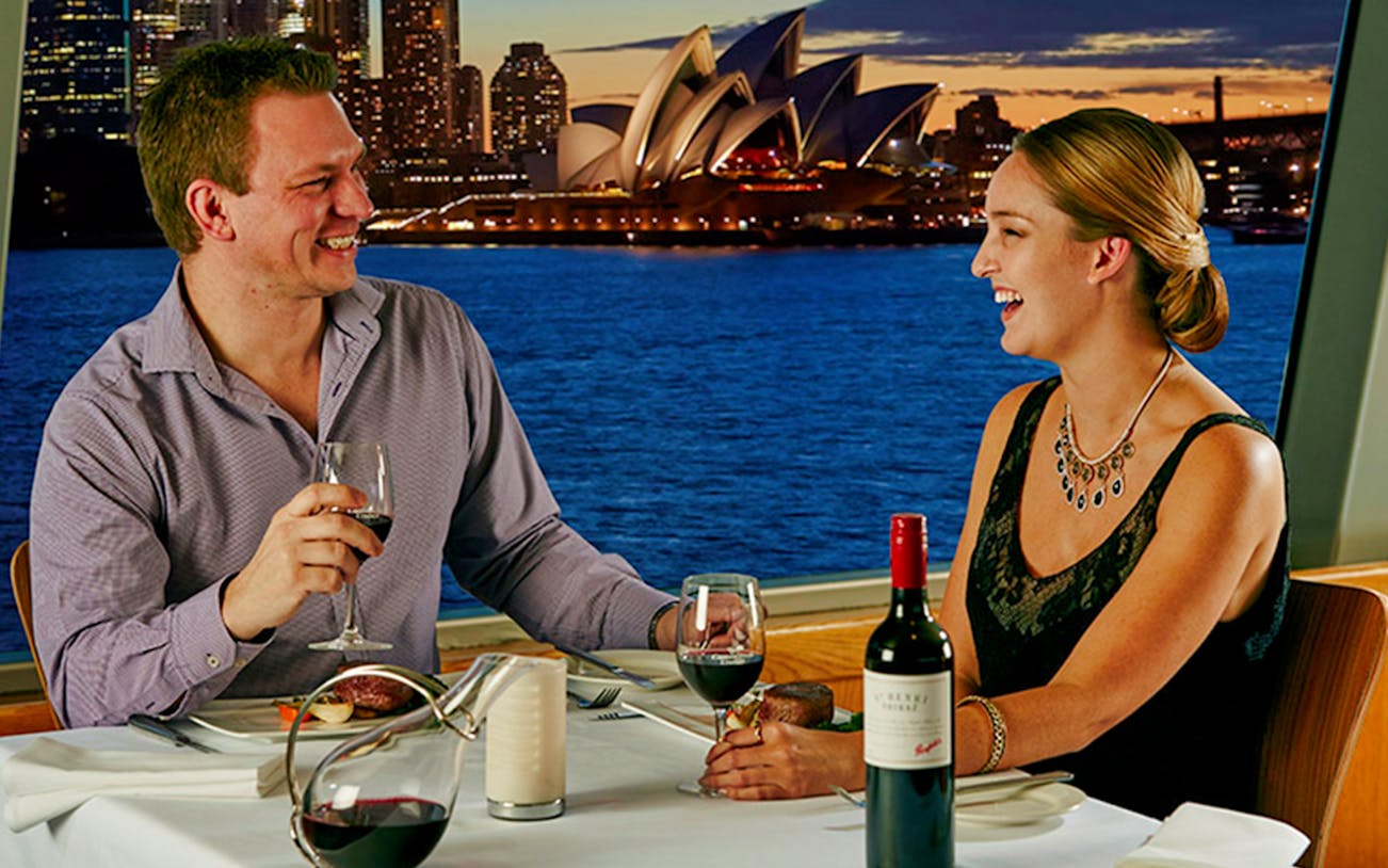 Couple dining with Penfolds Grange wine on luxury cruise, Sydney Opera House view.