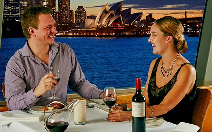 Couple dining with Penfolds Grange wine on luxury cruise, Sydney Opera House view.