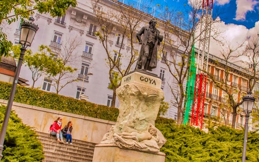 Goya statue near Prado Museum, Madrid, with visitors seated on steps.