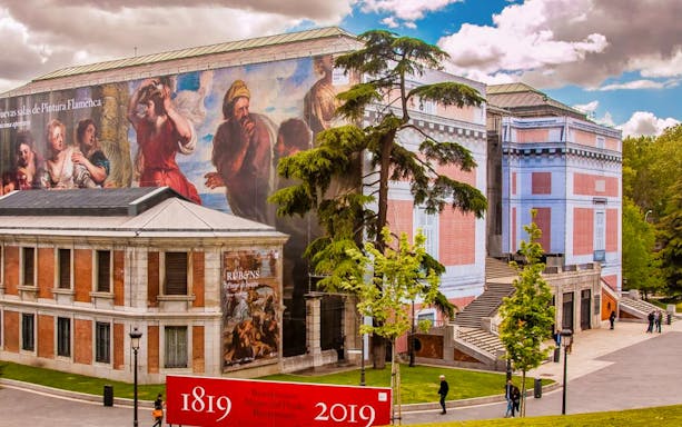 Prado Museum exterior with large mural and visitors in Madrid, Spain.
