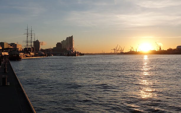 Sunrise over Elbe River near Altona Fish Market, Hamburg, with ships and cranes in view.