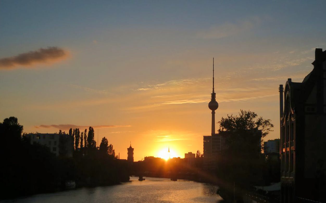 Berlin TV Tower silhouetted against sunset sky.