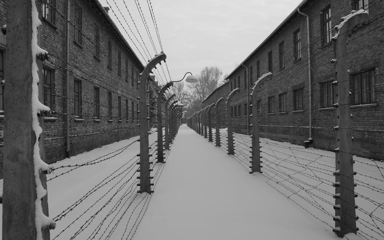 Barbed wire fences and brick buildings at Auschwitz Birkenau Museum in winter.