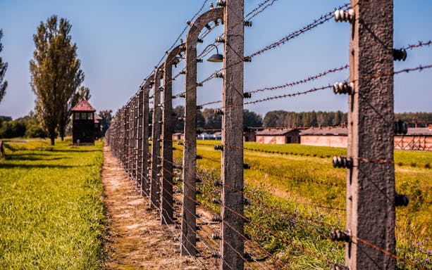 Barbed wire fence at Auschwitz Birkenau Museum, Poland, with watchtower in the background.