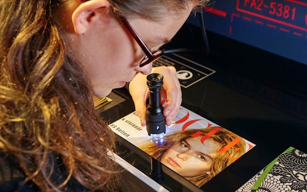 Person examining magazine with magnifying glass at German Spy Museum, Berlin.