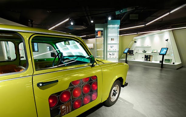 Yellow car exhibit at German Spy Museum, Berlin, with spy gadgets displayed in the background.