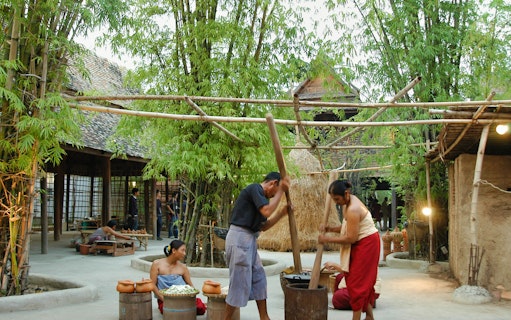 Traditional Thai village scene at Siam Niramit Bangkok with people engaging in cultural activities.