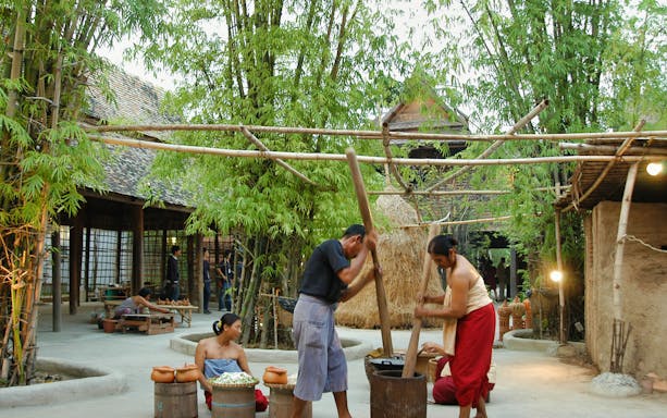 Traditional Thai village scene at Siam Niramit Bangkok with people engaging in cultural activities.