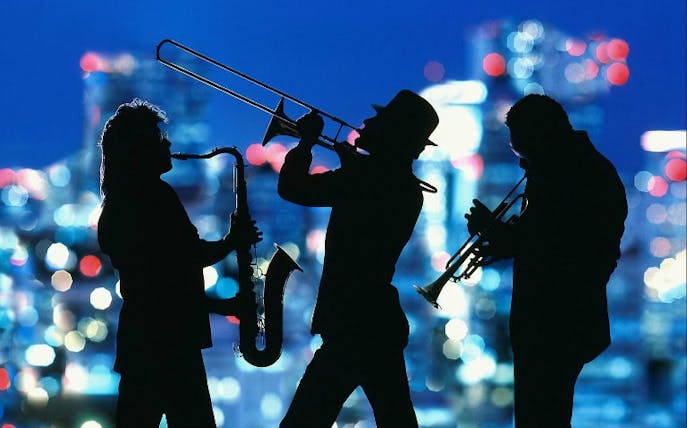 Silhouettes of jazz musicians playing saxophone, trombone, and trumpet against a city skyline.