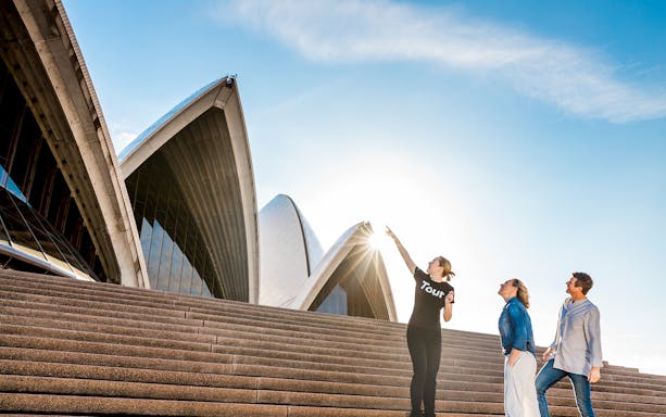 Tour guide showing visitors the Sydney Opera House steps under a clear sky.