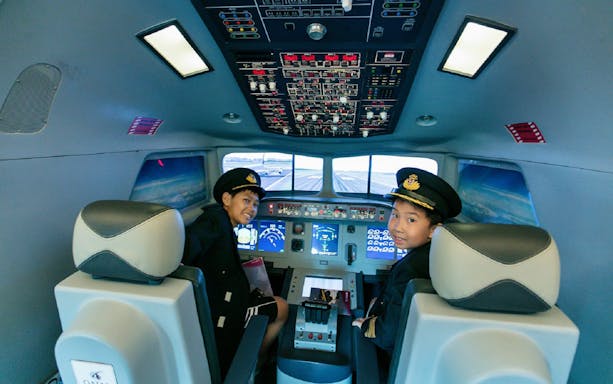 Children in pilot uniforms inside a flight simulator at Kidzania Bangkok.
